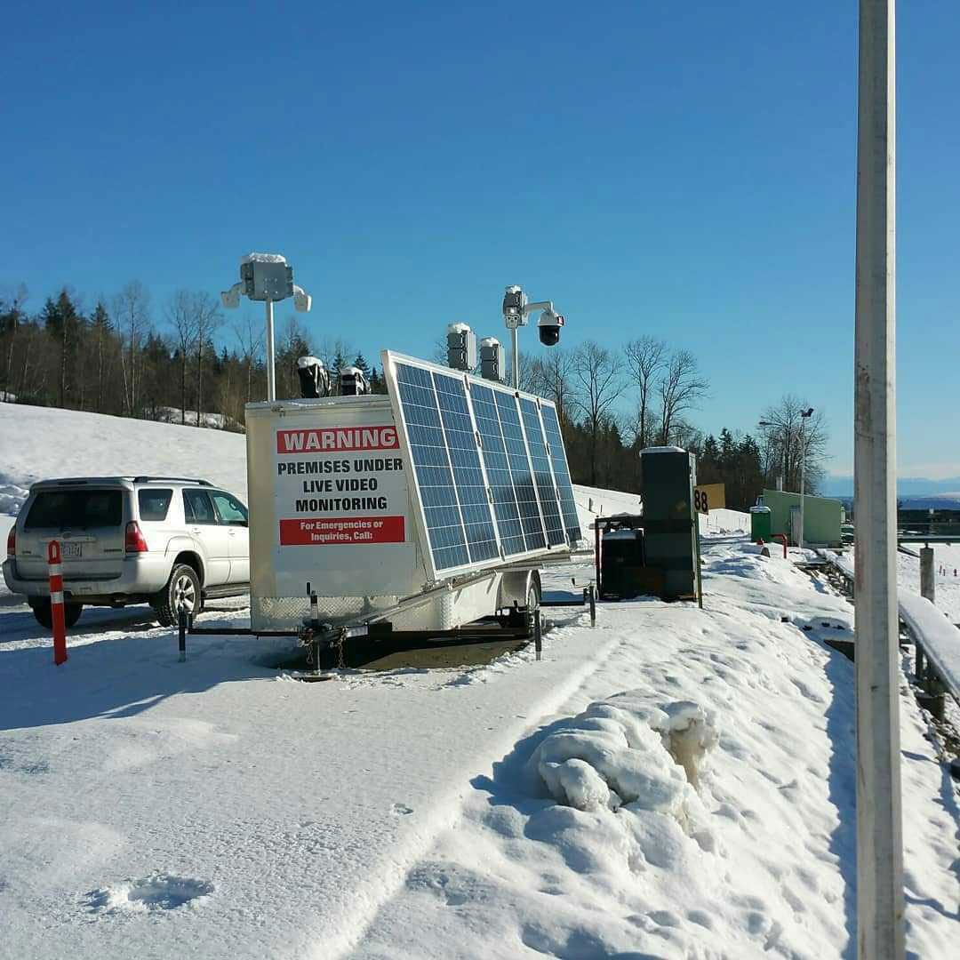 Mobile solar-powered surveillance unit on snowy terrain with a warning sign for live video monitoring.