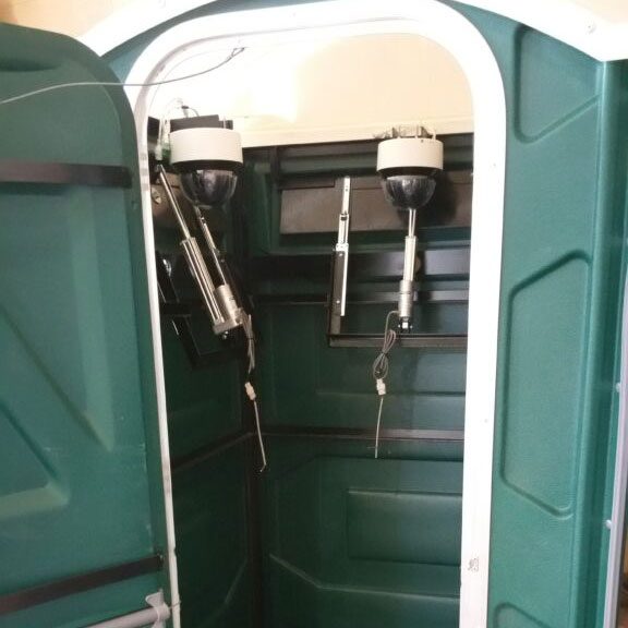 Interior of a portable toilet with hand sanitizer and a toilet paper dispenser.