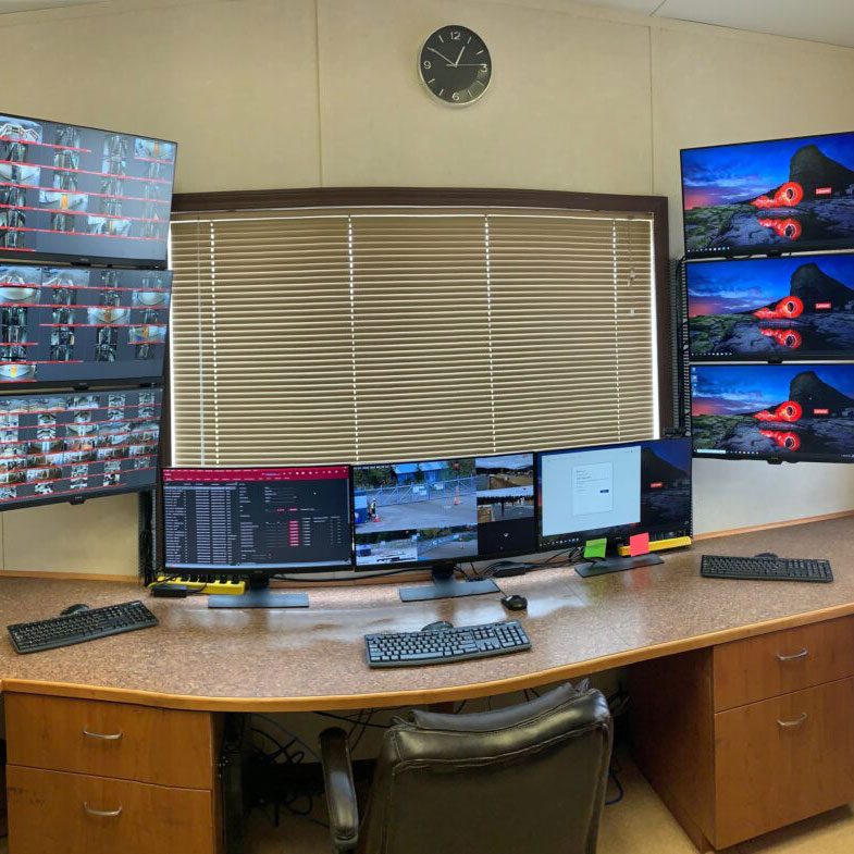 A security monitoring station with multiple screens displaying various camera feeds and computer interfaces.