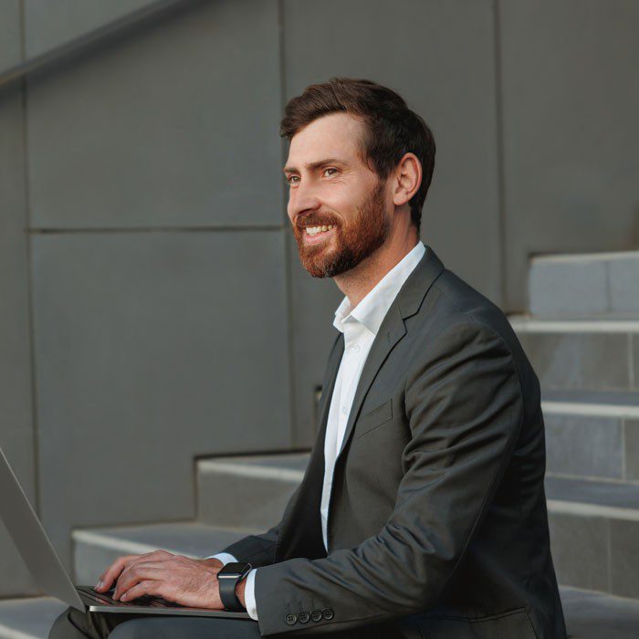 Man in a suit working on a laptop outdoors.