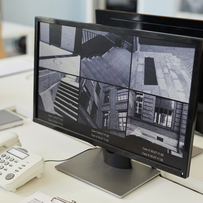 Computer monitor displaying a grid of security camera feeds on a desk with a telephone alongside.