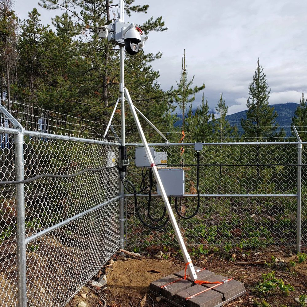 Weather monitoring station with instruments and fenced enclosure in a forested area.