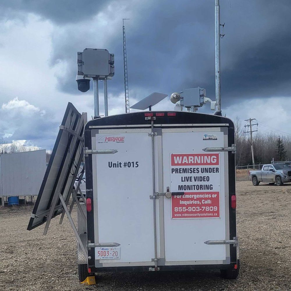 Mobile surveillance unit with warning sign about live video monitoring under a cloudy sky.