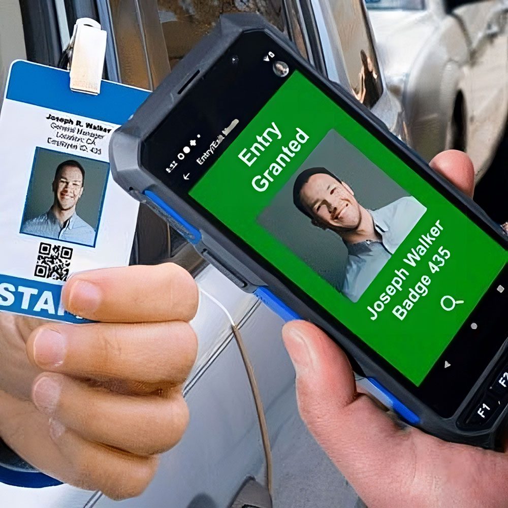 Hand holding a security badge scanner with a screen showing "entry granted" for an individual's identification card.