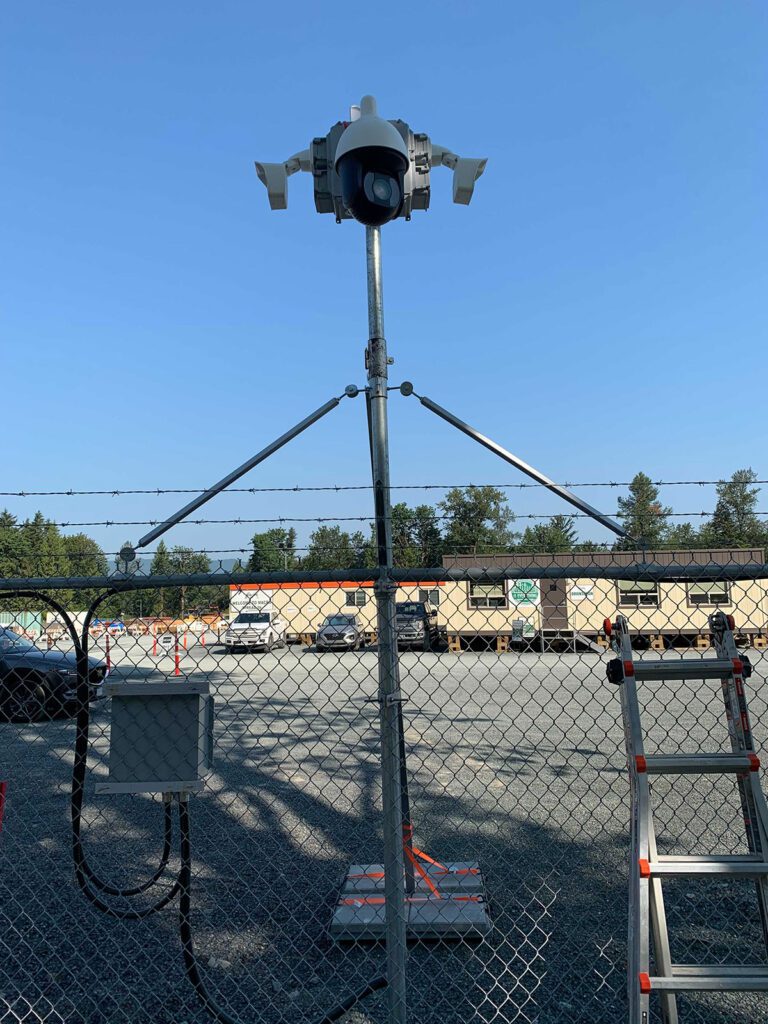 A mobile surveillance camera system mounted on a tripod overlooking a fenced area with a ladder in the foreground.