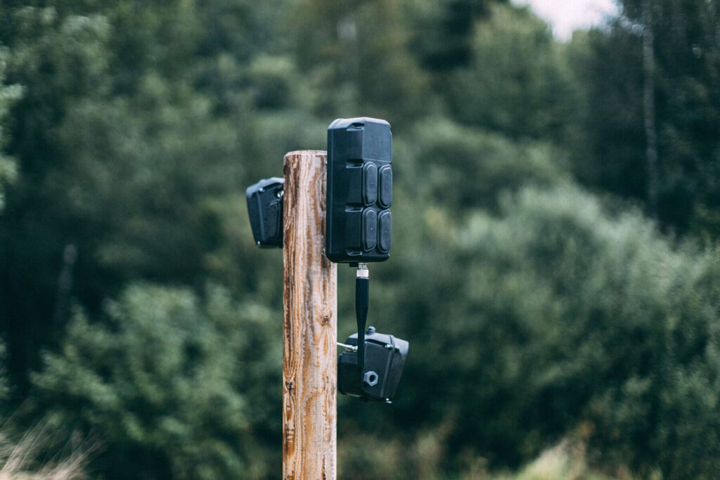 A trail camera mounted on a wooden post in a forested area.