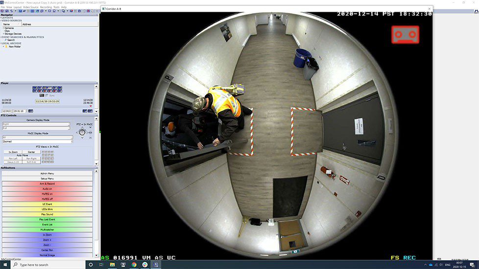 Security camera footage of a person in a yellow jacket walking through a curved corridor.