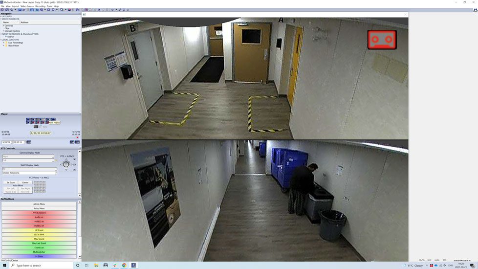 Security camera monitors displaying two different angles of an empty building corridor and a solitary individual in a maintenance or service role.