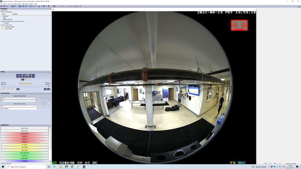 Security camera feed displaying a distorted wide-angle view of an office interior with monitors and desks, timestamped and monitored on a computer screen.