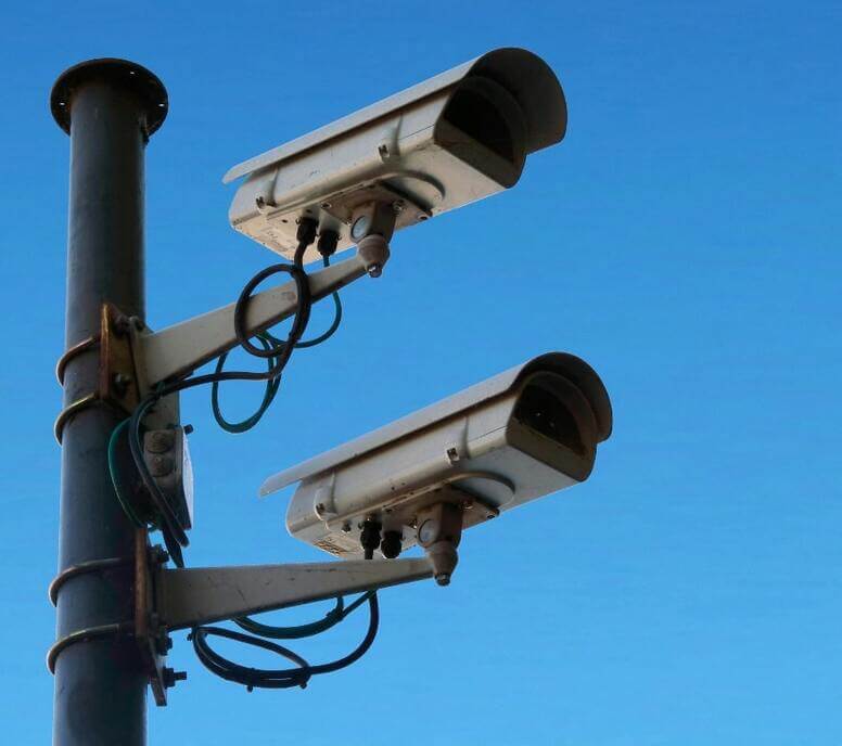 Two security cameras mounted on a pole against a clear blue sky
